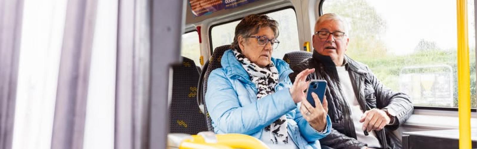 2 mensen in een lijnbus kijkend op gsm